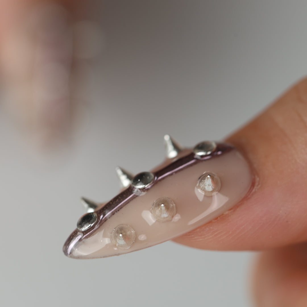 Silver Spine press-on nails close-up on finger with nude base, silver spikes, and raised metallic studs