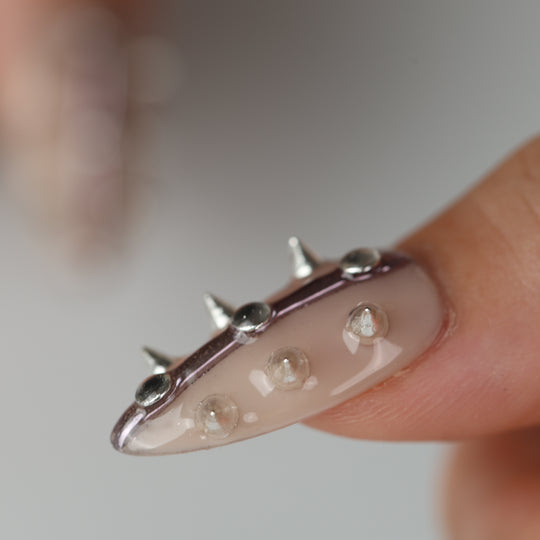 Silver Spine press-on nails close-up on finger with nude base, silver spikes, and raised metallic studs