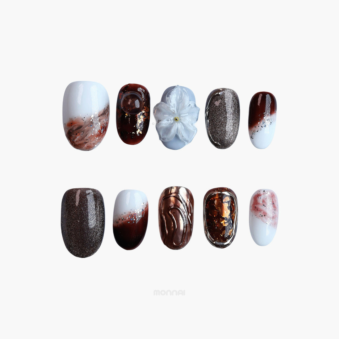 Smoky Quartz press-on nails laid out in moody espresso, frosted white, and silver cat-eye textures with sculpted flower detail.