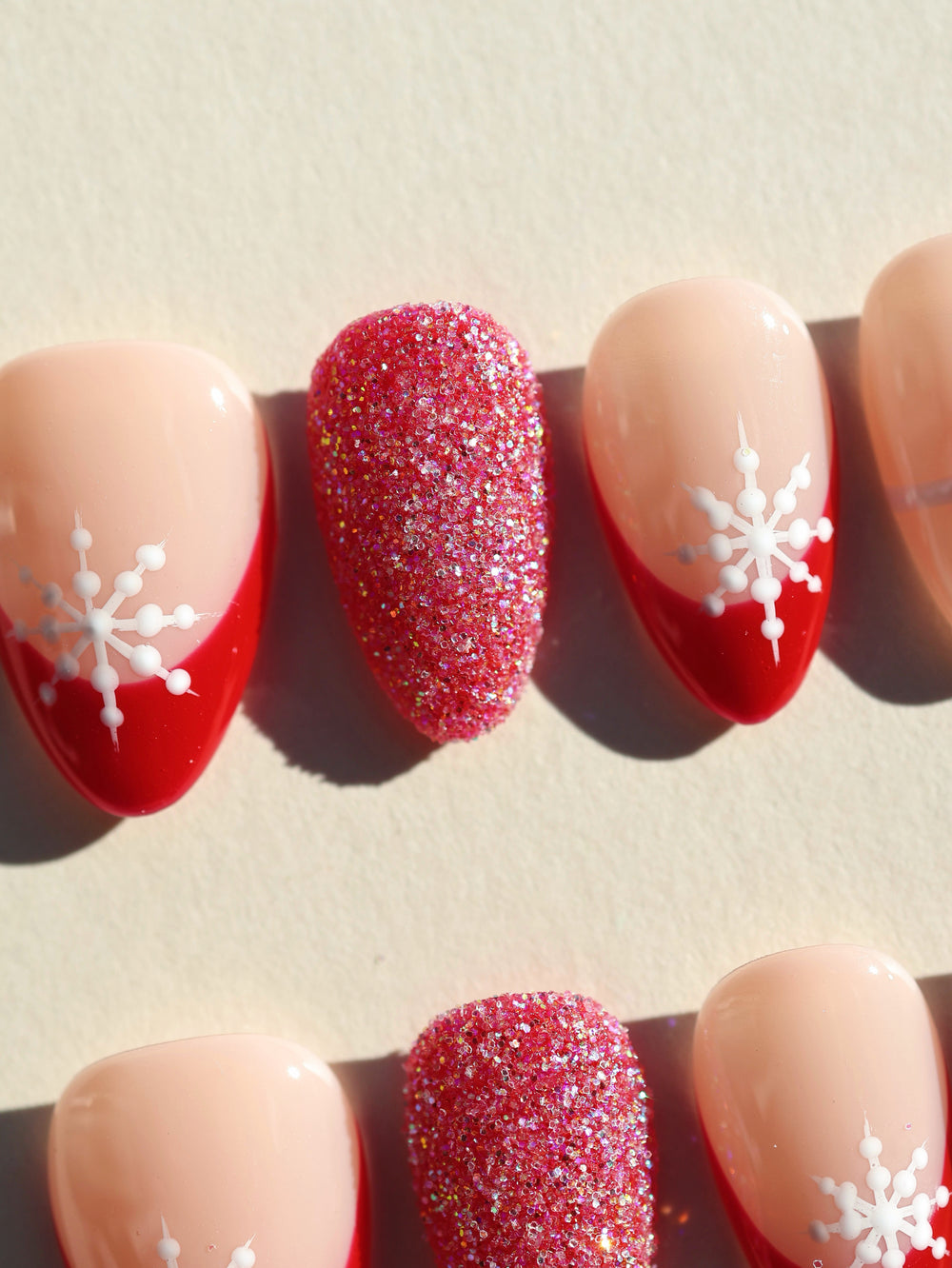Snowflake Gift Christmas-themed press-on nails laid out, featuring red French tips, white snowflakes, and a glitter accent nail.
