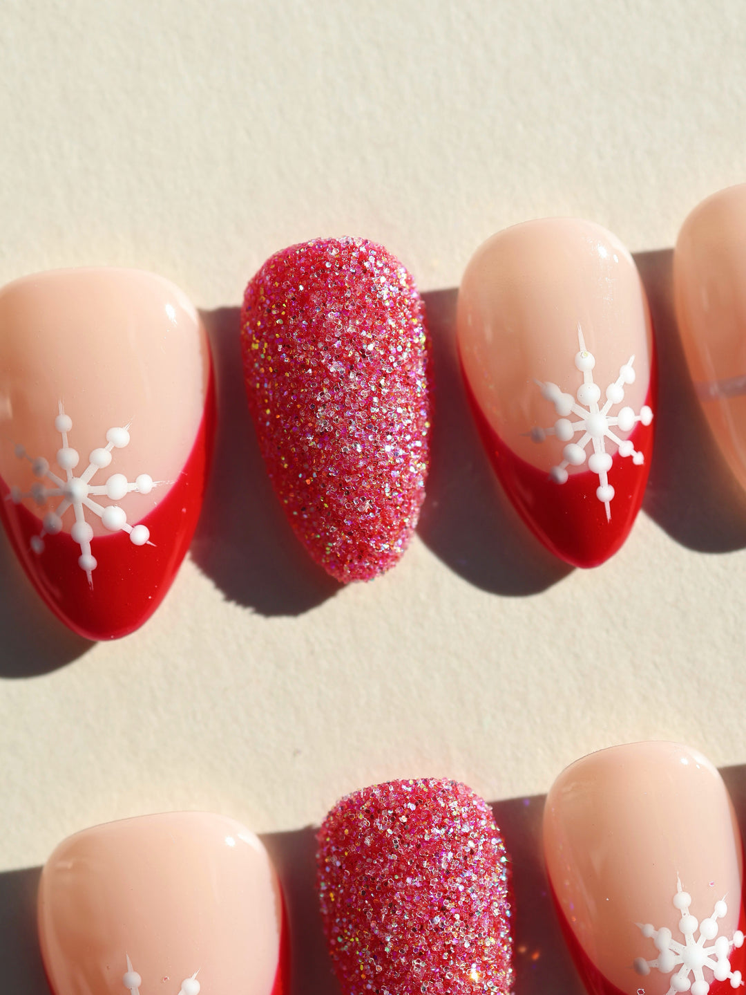 Snowflake Gift Christmas-themed press-on nails laid out, featuring red French tips, white snowflakes, and a glitter accent nail.