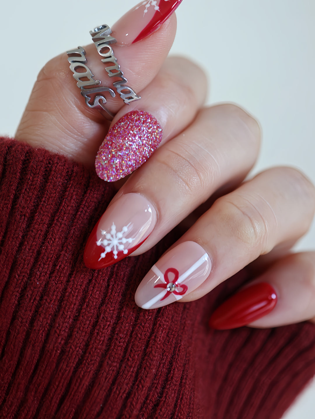 Snowflake Gift Christmas-themed press-on nails on hand with red French tips, a glitter accent nail, and snowflake detail.