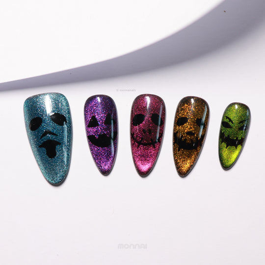 Spooky Spark press-on nails laid out, showing shimmering multicolor cat eye bases with hand-painted spooky Halloween faces.