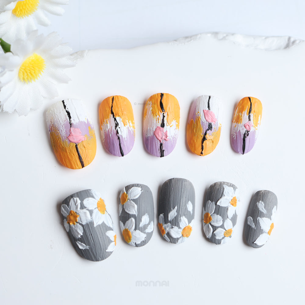 Spring on Canvas press-on nails laid out in close-up, with painterly grey floral details and layered orange, lilac, and white brushstrokes.