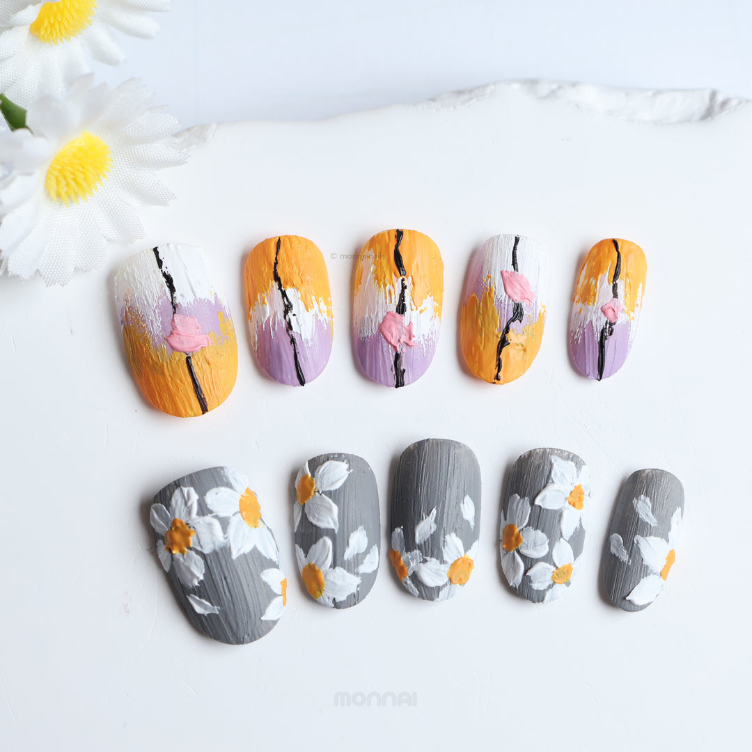 Spring on Canvas press-on nails laid out in close-up, with painterly grey floral details and layered orange, lilac, and white brushstrokes.