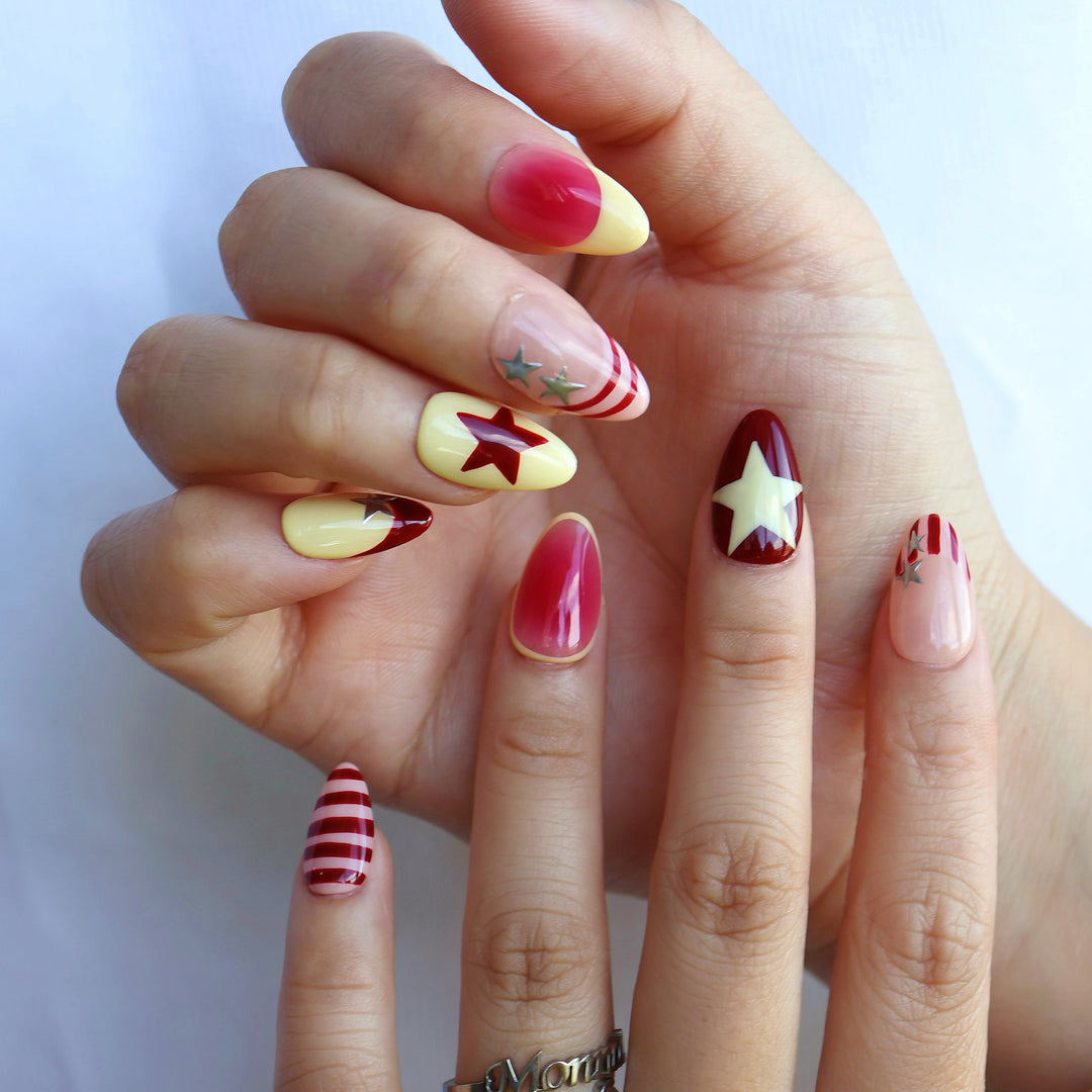 Star Parade press-on nails worn on hands, with red aura gradients, butter yellow accents, silver stars, and striped gel-gloss finish.