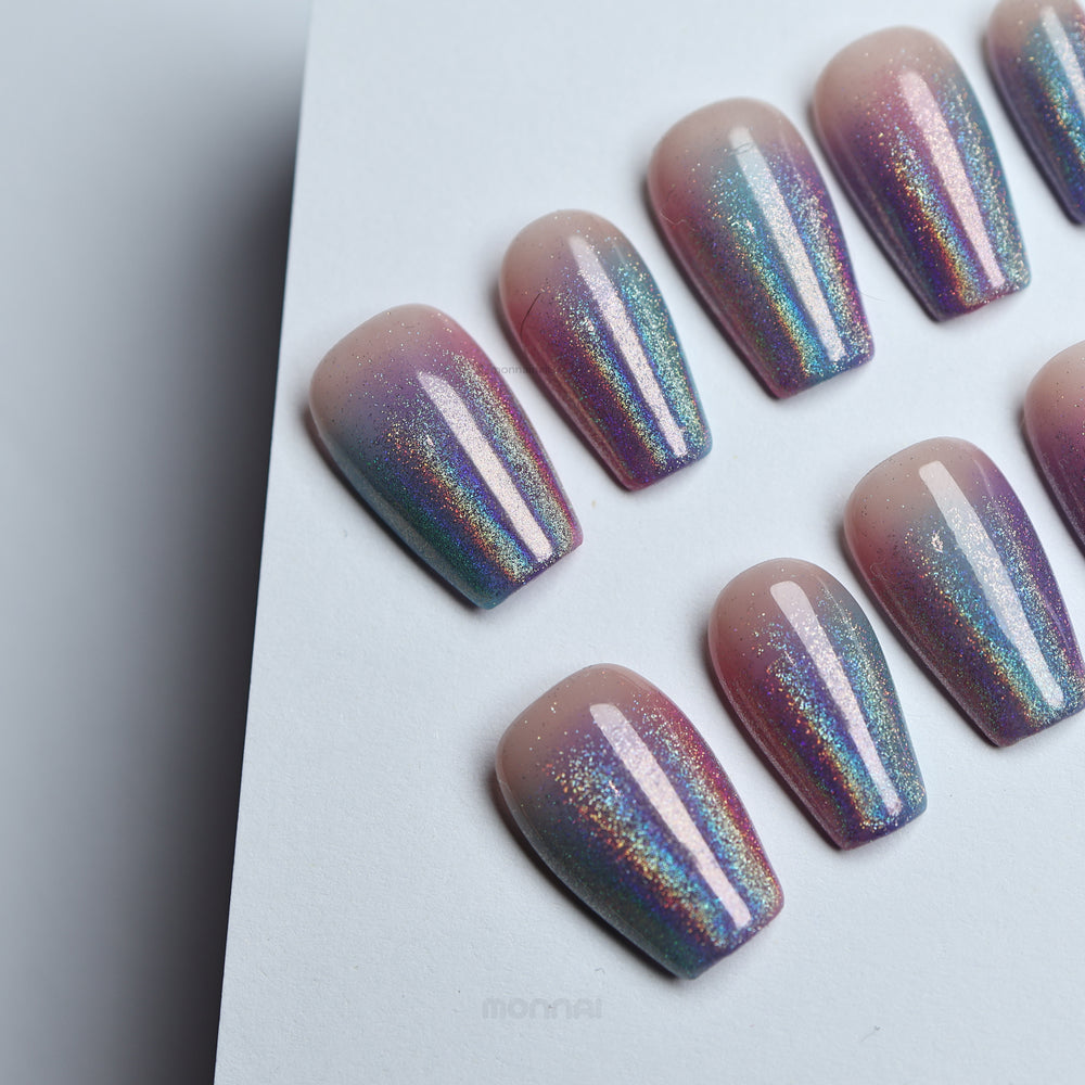 Stardust press-on nails laid out with soft nude base and pink-blue glitter ombré, high-shine finish