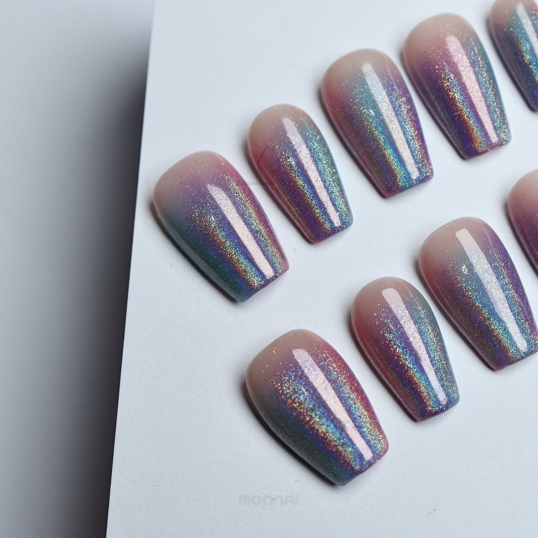 Stardust press-on nails laid out with soft nude base and pink-blue glitter ombré, high-shine finish