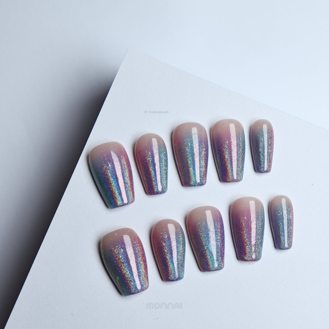 Stardust press-on nails with nude bases and pink-blue glitter ombré, shown laid out in two rows.