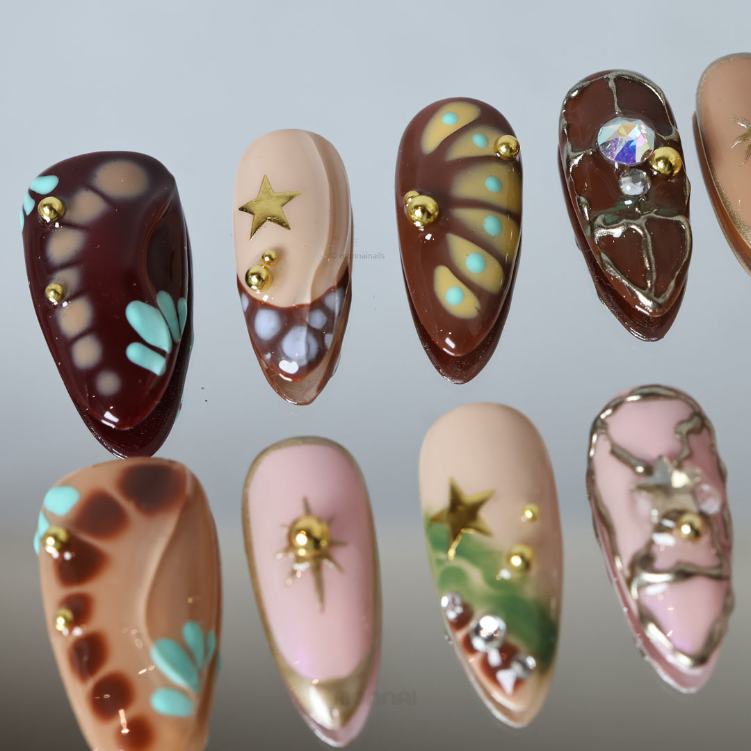 Starlit Glow press-on nails in retro playful nude, brown and metallic star designs with crystal details, laid out in close-up.
