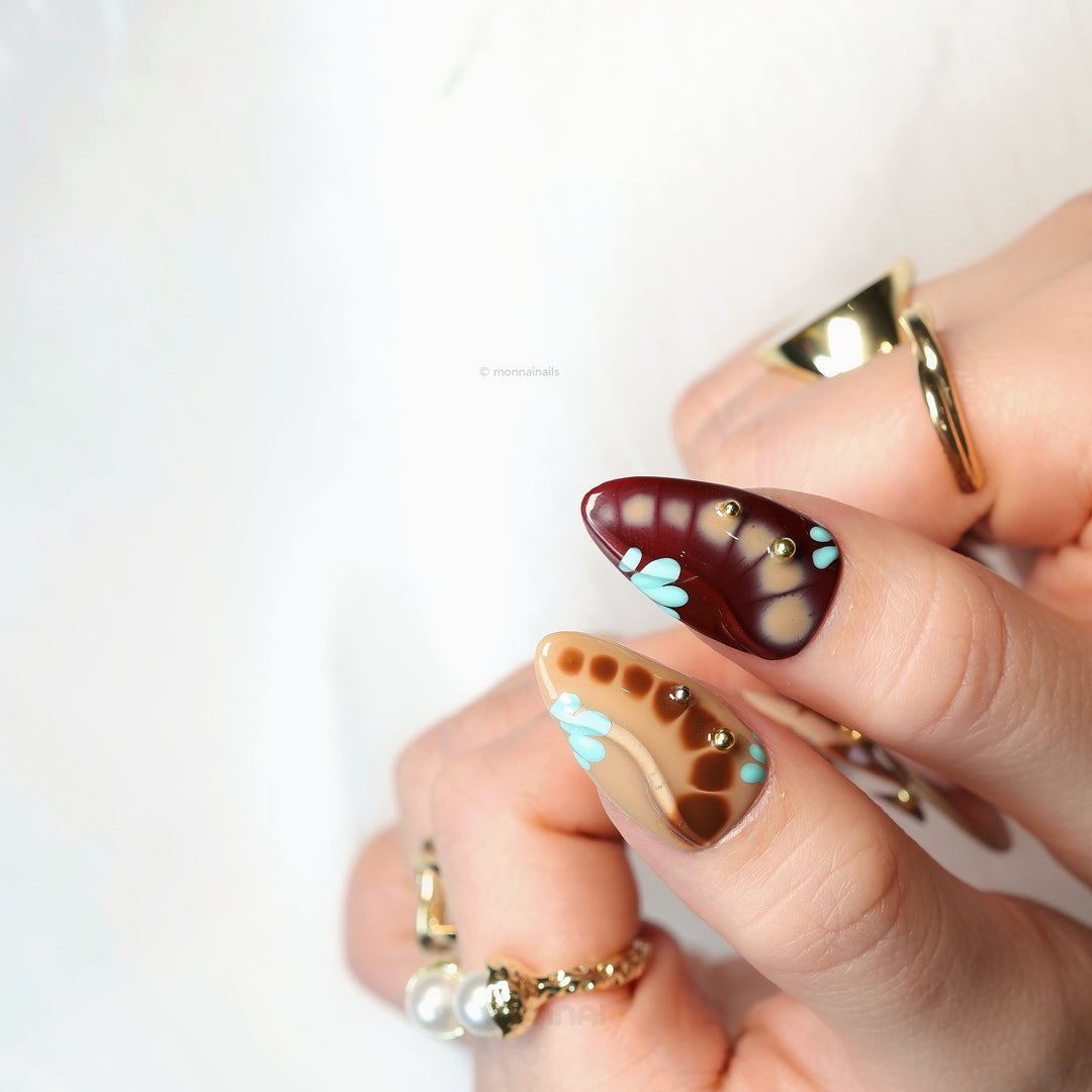 Starlit Glow press-on nails worn on hand, retro mix with nude and brown tones, metallic accents and small crystal details.
