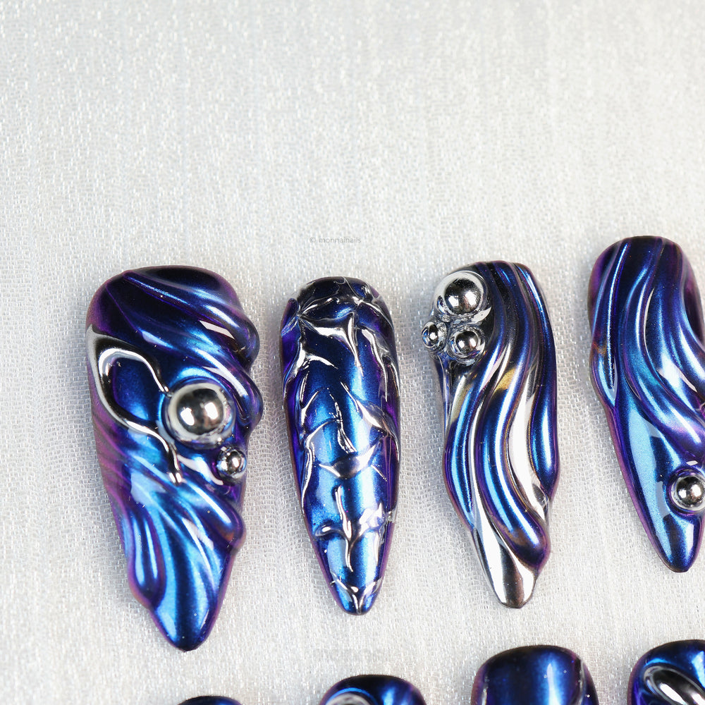 Stellar Ripples press-on nails with electric blue chrome and silver metallic wave details, shown laid out in close-up