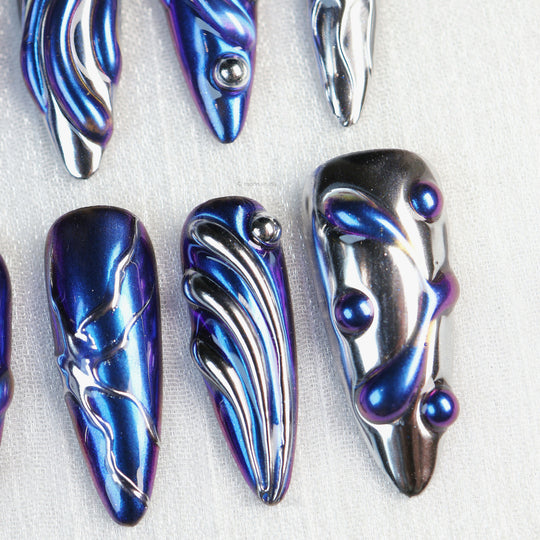 Stellar Ripples press-on nails laid out in close-up, with electric blue chrome and silver wave detailing.