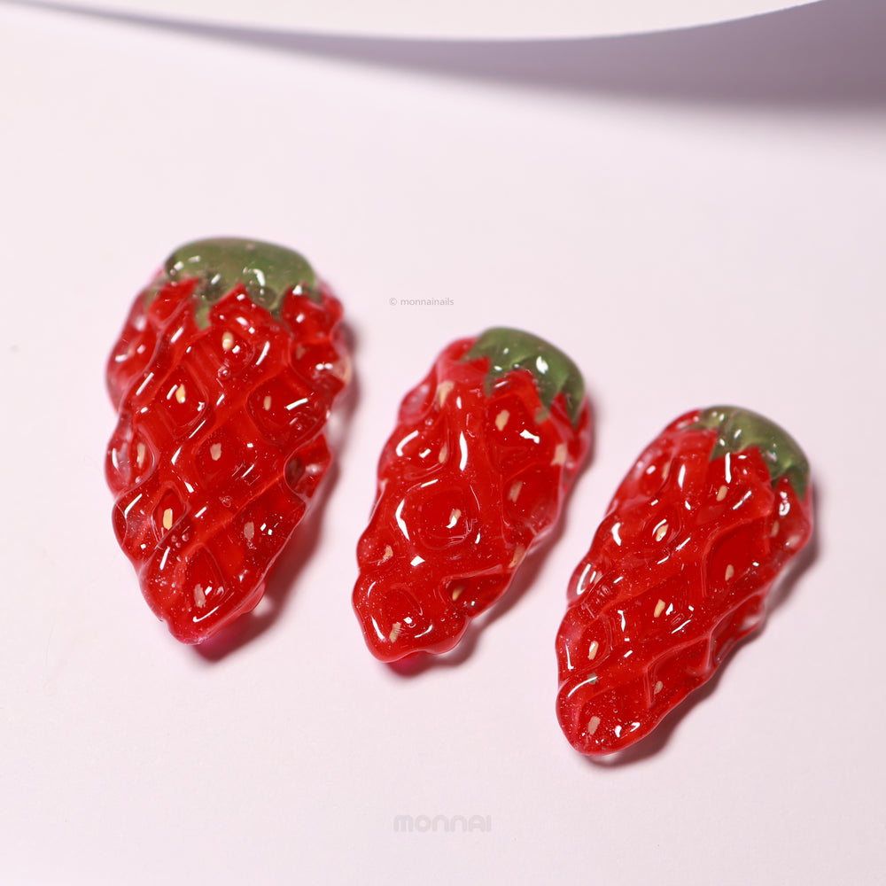 Strawberry Delight press-on nails laid out in close-up, with hyper-realistic red strawberry texture and green leafy tops
