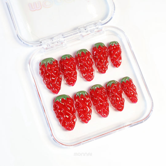 Strawberry Delight press-on nails in a clear case, showing hyper-realistic 3D strawberry nails with glossy red finish and green leafy tops.