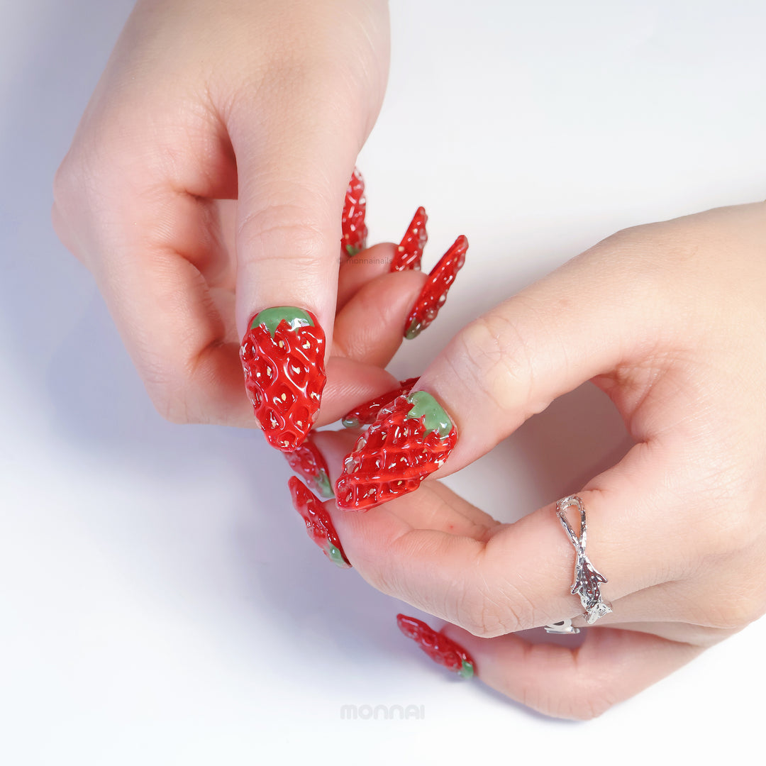 Strawberry Delight press-on nails worn on hands, showing hyper-realistic 3D strawberry texture in glossy red with green leafy stems.