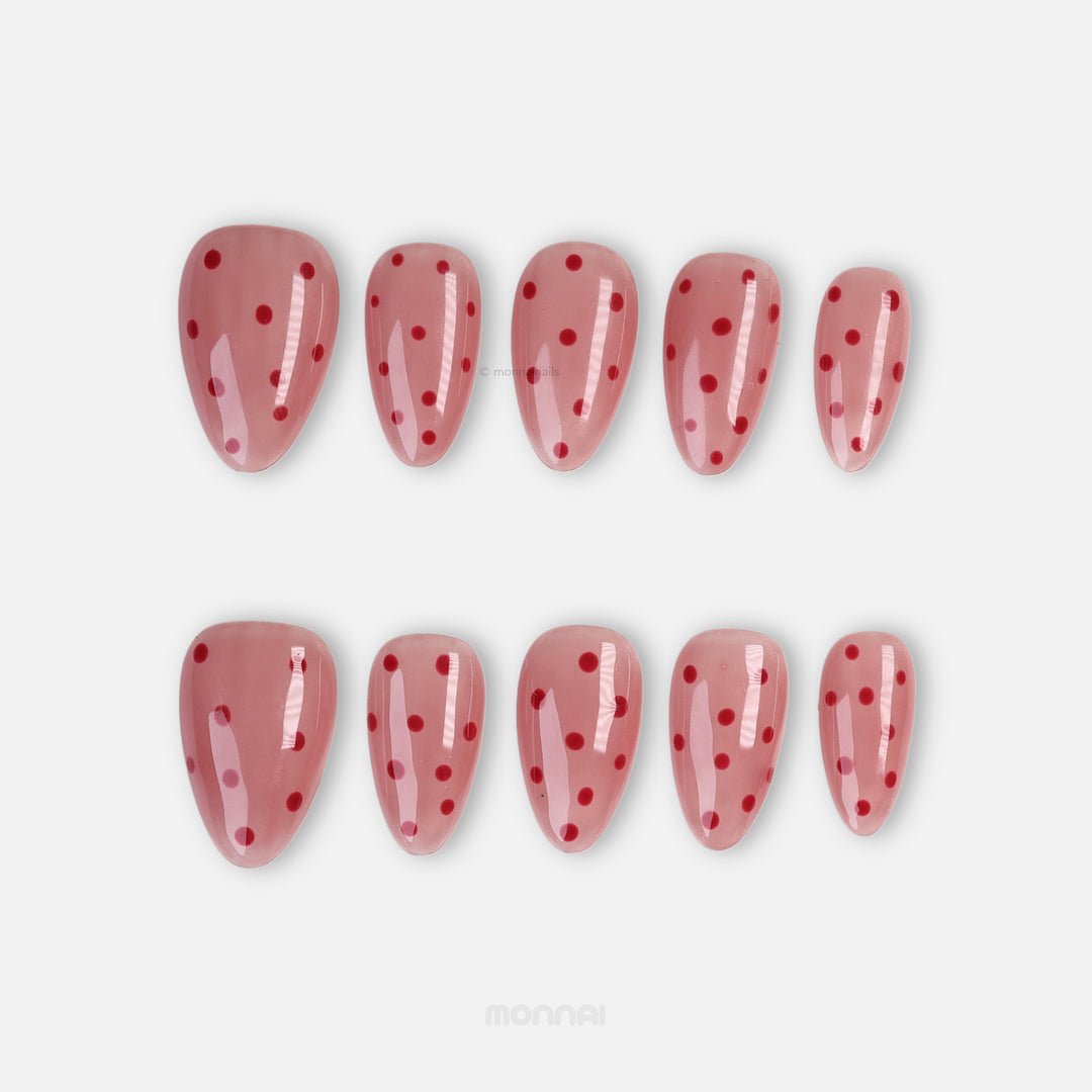 Strawberry Mousse press-on nails with red polka dots on a glossy nude pink base, shown laid out in two rows