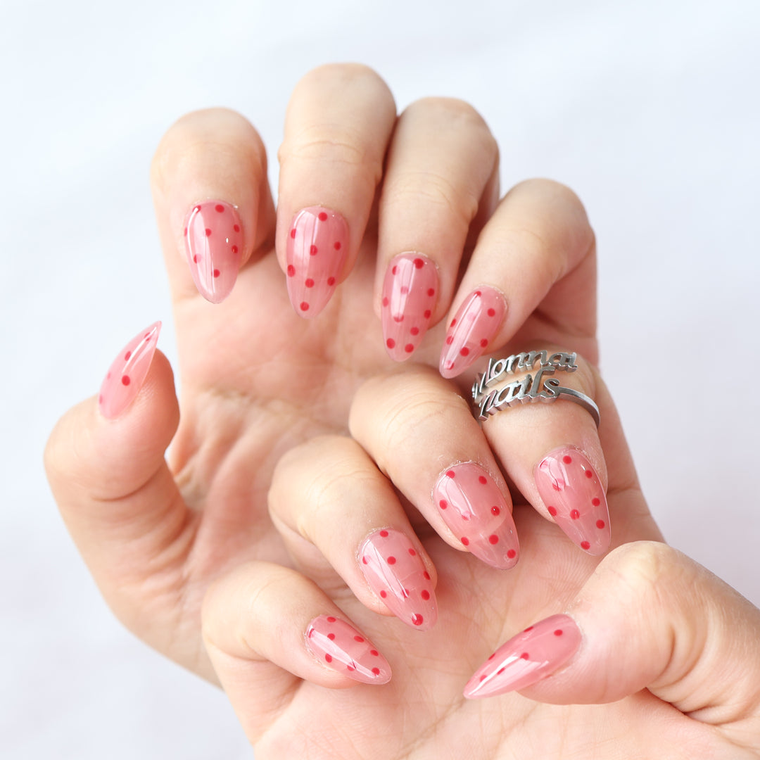 Strawberry Mousse press-on nails worn on hand, pink jelly base with red polka dots and glossy finish
