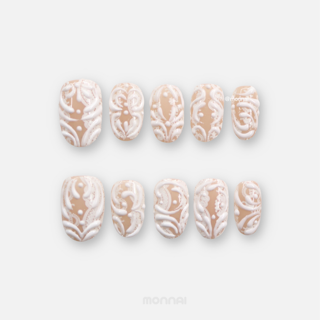 Sugar Carving press-on nails set with sheer nude base, white 3D swirls, and lace details laid out on white