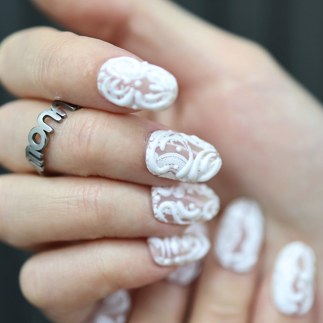 Sugar Carving press-on nails on hand with sheer nude base, white lace swirls, and glossy finish