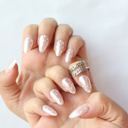 Sugar Glaze press-on nails worn on hands, sheer champagne pink with white polka dots and a pearlescent shimmer.