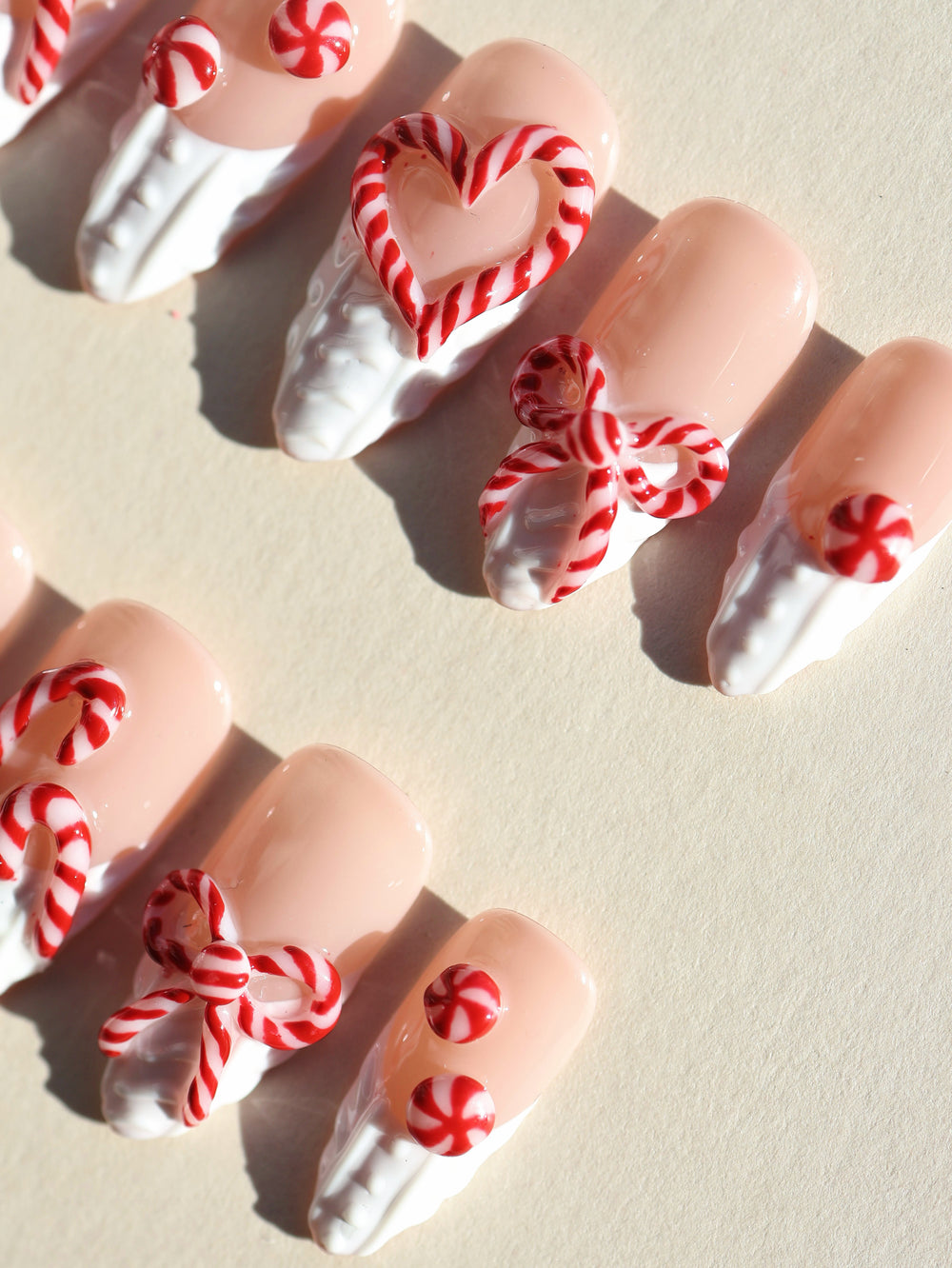 Sugar Kiss press-on nails laid out with nude bases, white 3D knit texture, and red candy cane hearts and bows.