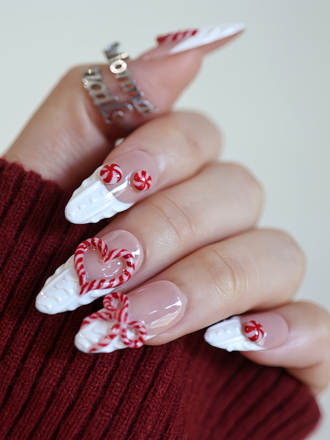 Sugar Kiss press-on nails on hand with nude base, white 3D knit texture, and red candy cane heart and bow details.