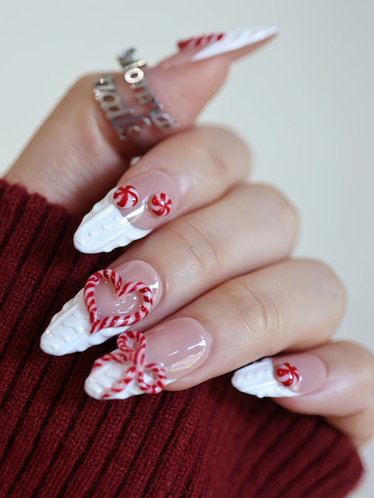 Sugar Kiss press-on nails on hand with nude base, white 3D knit texture, and red candy cane heart and bow details.