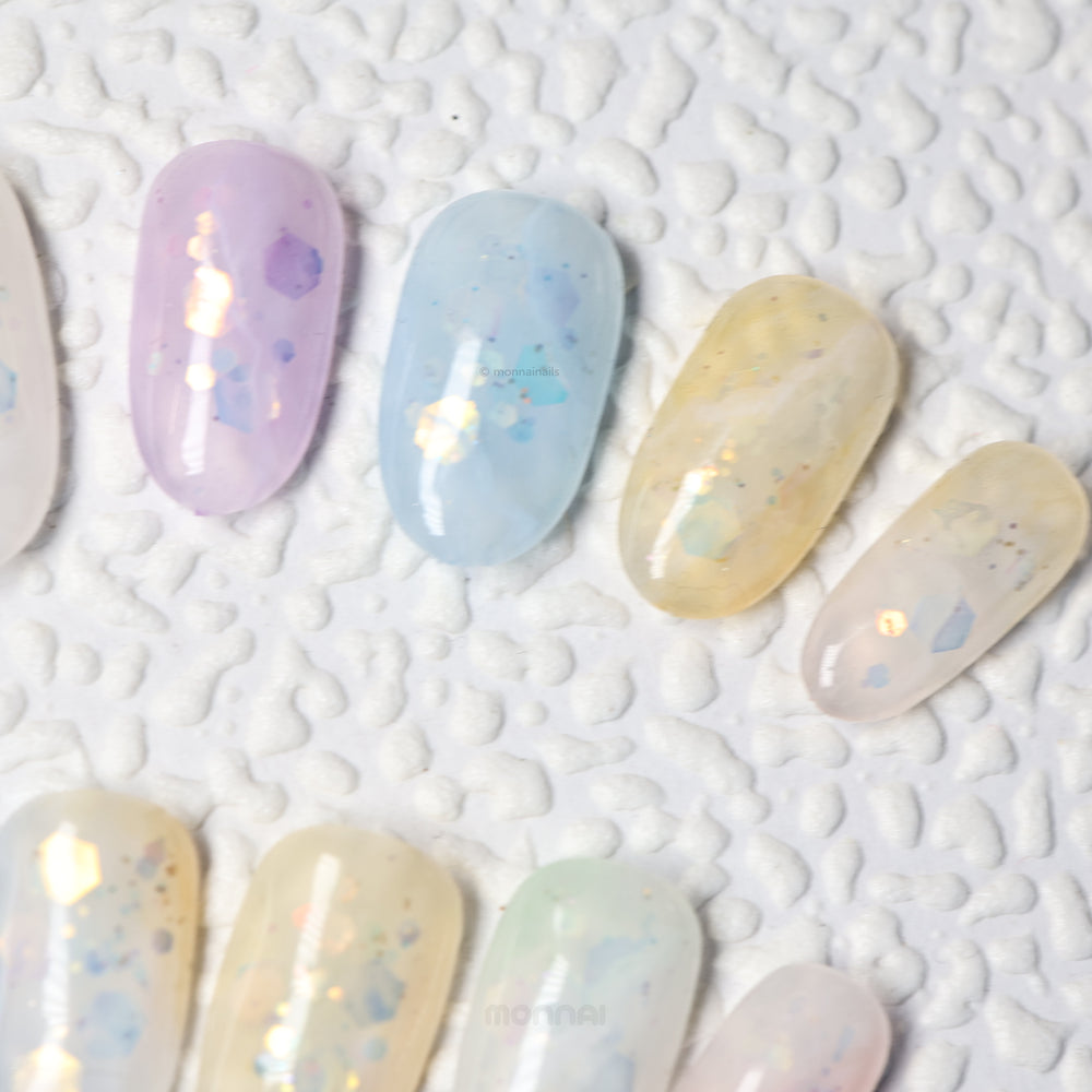 Sugar Sparkle press-on nails in pastel lavender, blue and yellow with airy shimmer and foil accents, laid out in close-up