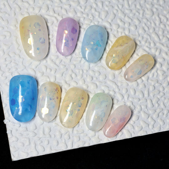 Sugar Sparkle press-on nails laid out in pastel blue, lavender, yellow and pink with airy shimmer and foil accents