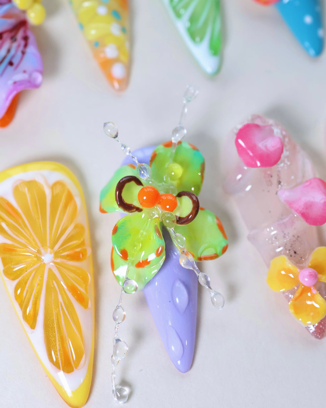 Summer Garden Party press-on nails laid out with neon floral, citrus slice and clear dew drop 3D accents