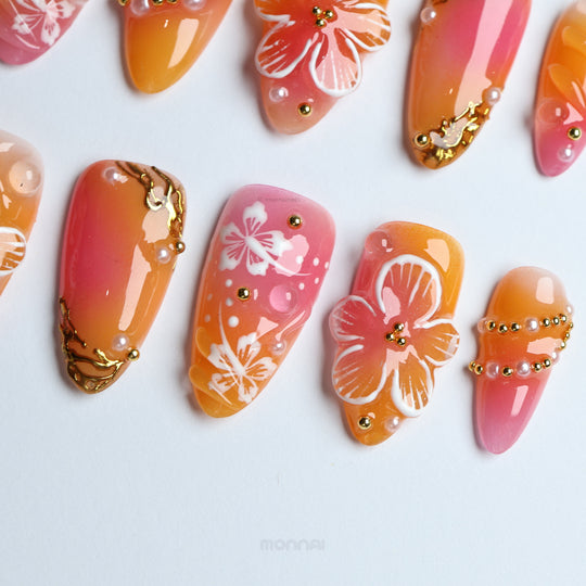 Sunset Hibiscus press-on nails laid out with pink-orange ombré fades, white floral details, and gold accents