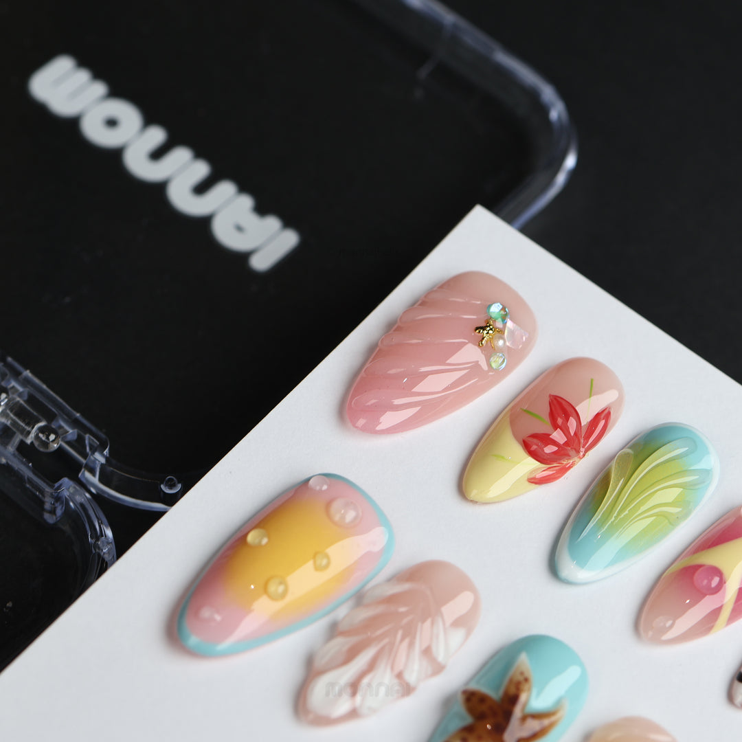 The Beach press-on nails laid out in close-up, with pink, blue, and yellow tropical designs and 3D shell accents.