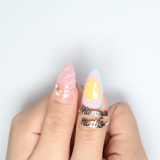 The Beach press-on nails worn on hand, showing pink shell texture, pastel gradient, and glossy droplets.