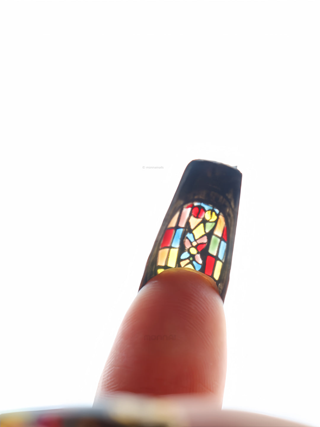 The Fifth Window press-on nails in close-up, showing a stained-glass motif with bold colorful panels and dark framed edges.