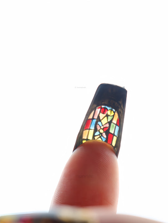 The Fifth Window press-on nails in close-up, showing a stained-glass motif with bold colorful panels and dark framed edges.