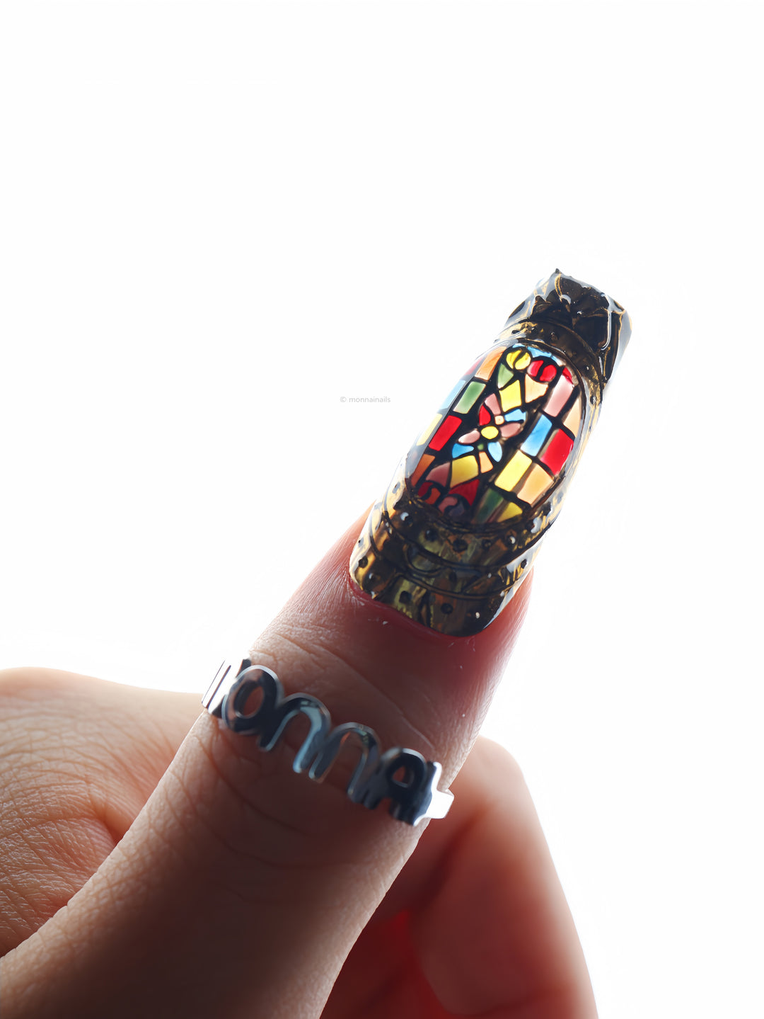 The Fifth Window press-on nails shown on a hand, with colorful stained-glass motifs in sculpted bronze frames.