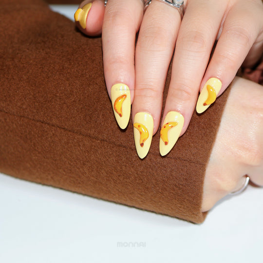 Tropical Banana press-on nails worn on hand, creamy pale yellow with hand-painted banana art and high-shine gloss.