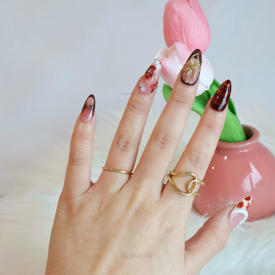 Twilight Shine press-on nails worn on hand, with sheer pink tones, tortoiseshell accents, and gold floral details.