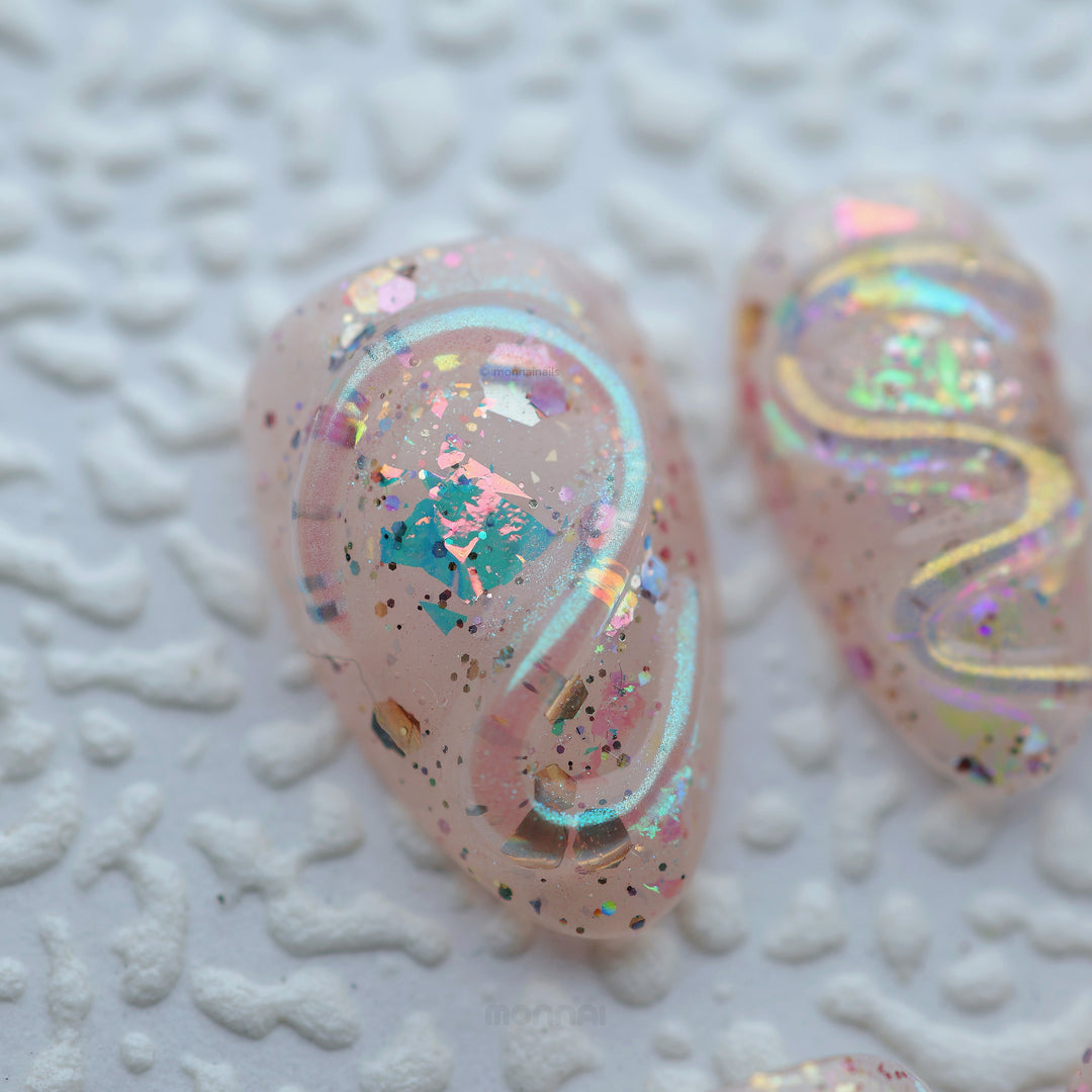 Twinkle press-on nails in close-up, sheer nude with iridescent glitter, glossy sculpted texture, and rainbow shimmer