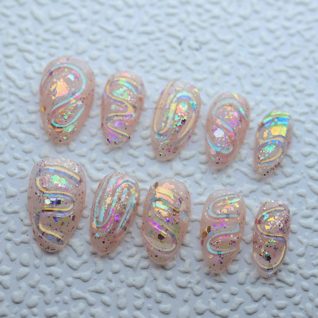 Twinkle press-on nails laid out, sheer nude with iridescent glitter and glossy sculpted swirl texture