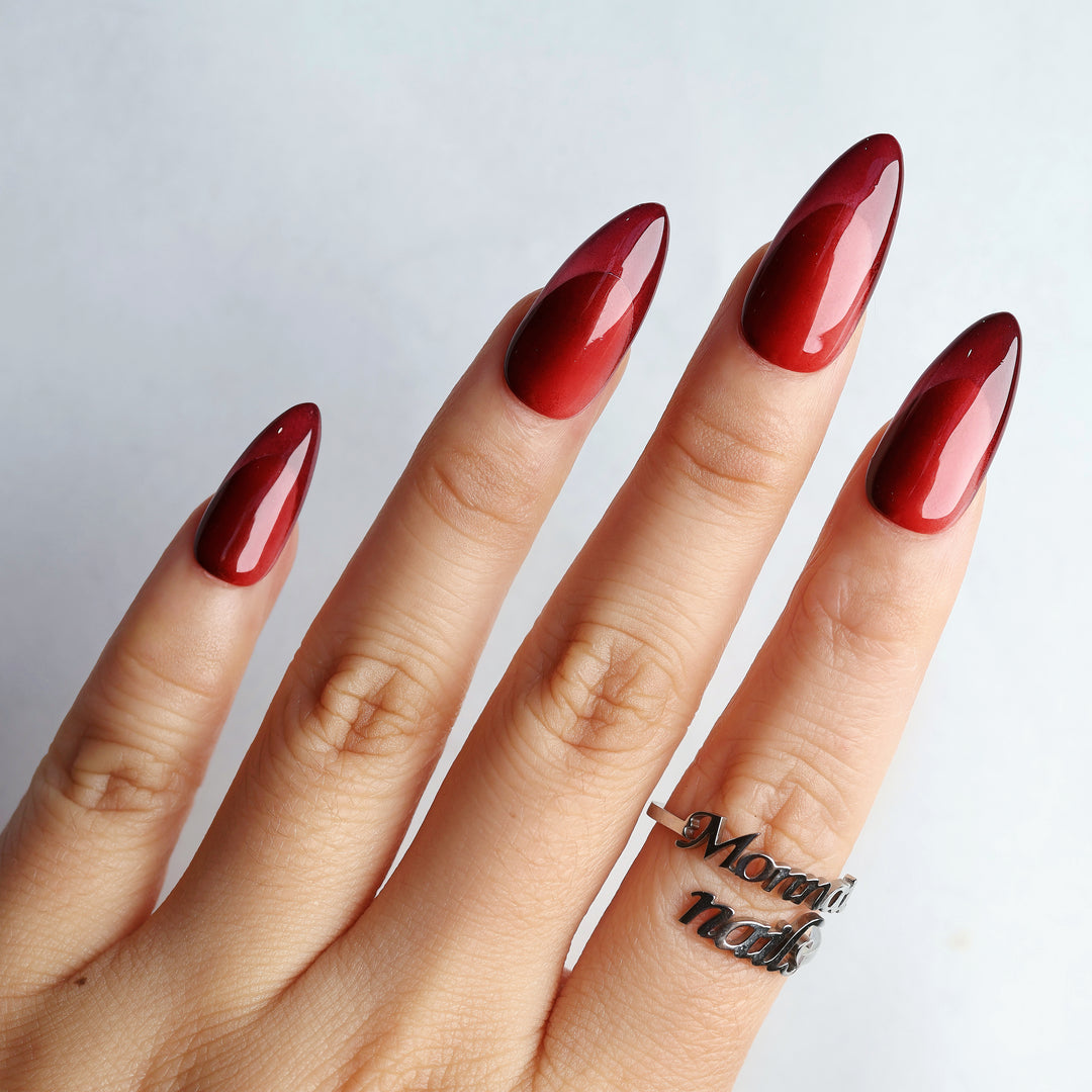 Vampire’s Kiss press-on nails on hand, deep red monochromatic glossy almond nails with a high-shine finish.