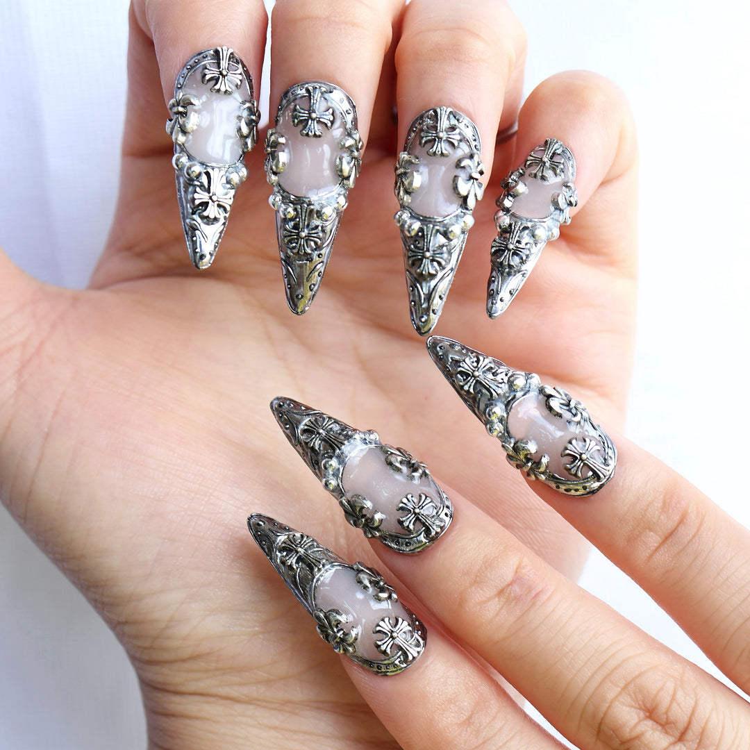 Veil gothic press-on nails worn on hand with silver metallic frames, creamy white base, and cross emblems