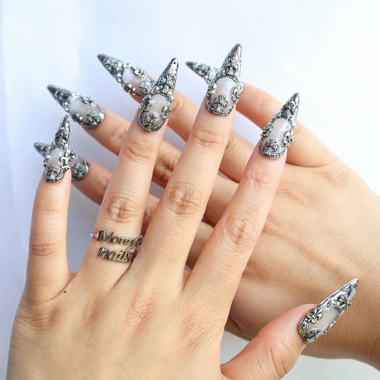 Veil press-on nails shown on hands, with sculpted silver gothic crosses over a creamy white base.