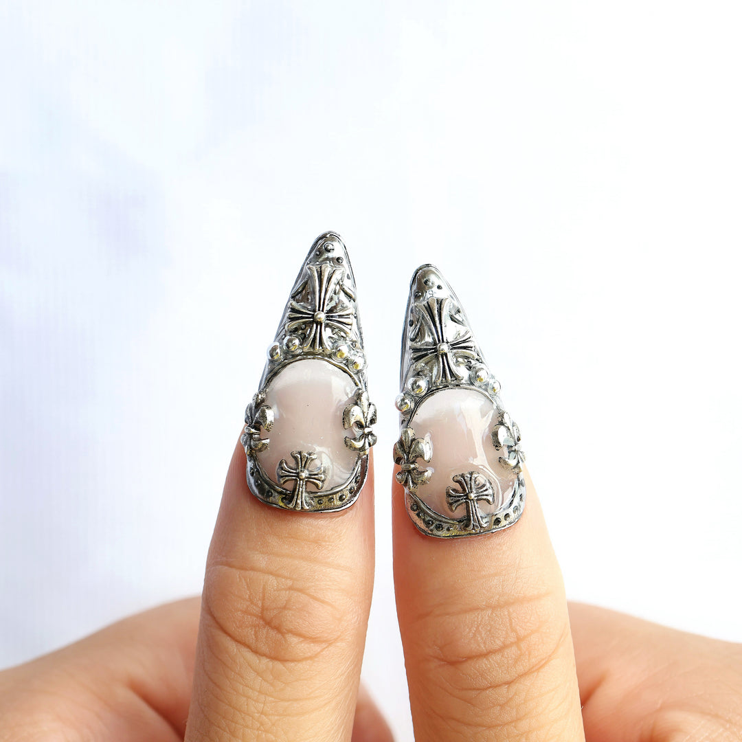 Veil press-on nails worn on fingers, with gothic silver frames and cross emblems over a creamy white base.