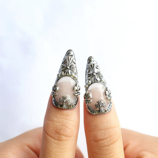 Veil press-on nails worn on fingers, with gothic silver frames and cross emblems over a creamy white base.