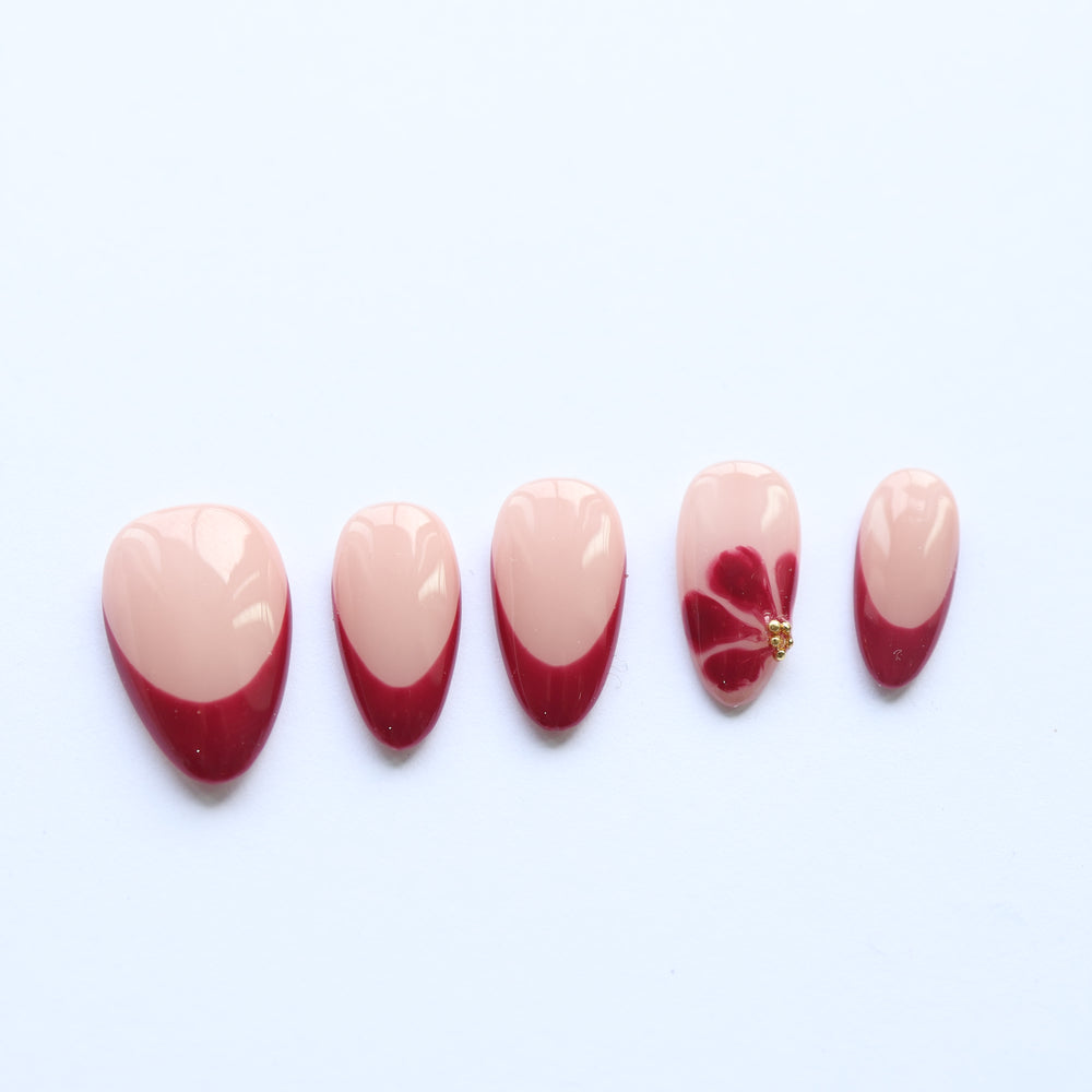 Velvet Petal press-on nails laid out with sheer nude bases, deep burgundy tips, and one floral accent with gold studs.