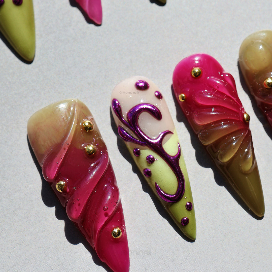 Vine press-on nails laid out with Y2K swirls, metallic purple lines, gold studs, and cool pink and olive tones.