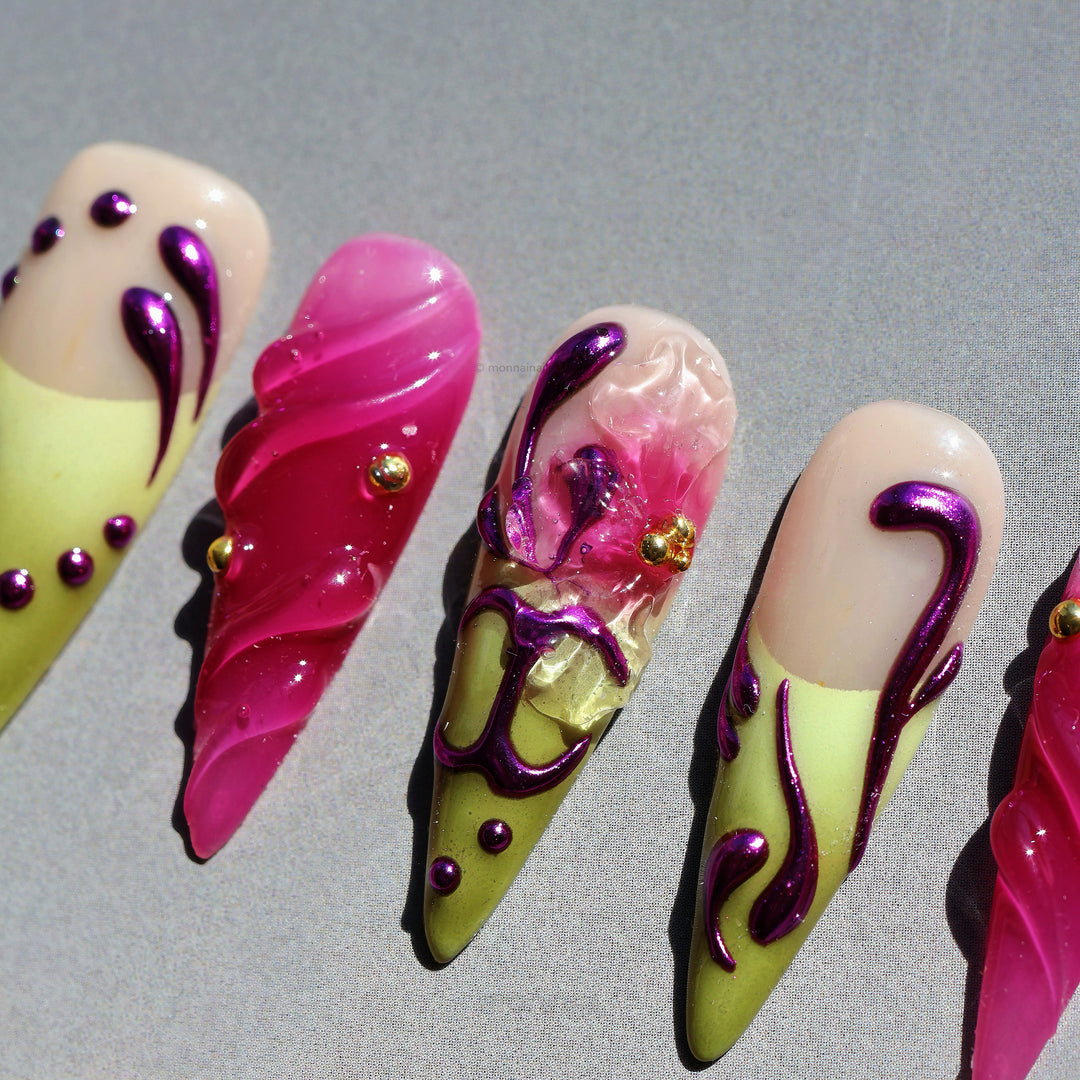 Vine press-on nails in close-up, laid out with sheer nude, pink, and olive tones, glossy purple swirls, and gold stud accents.