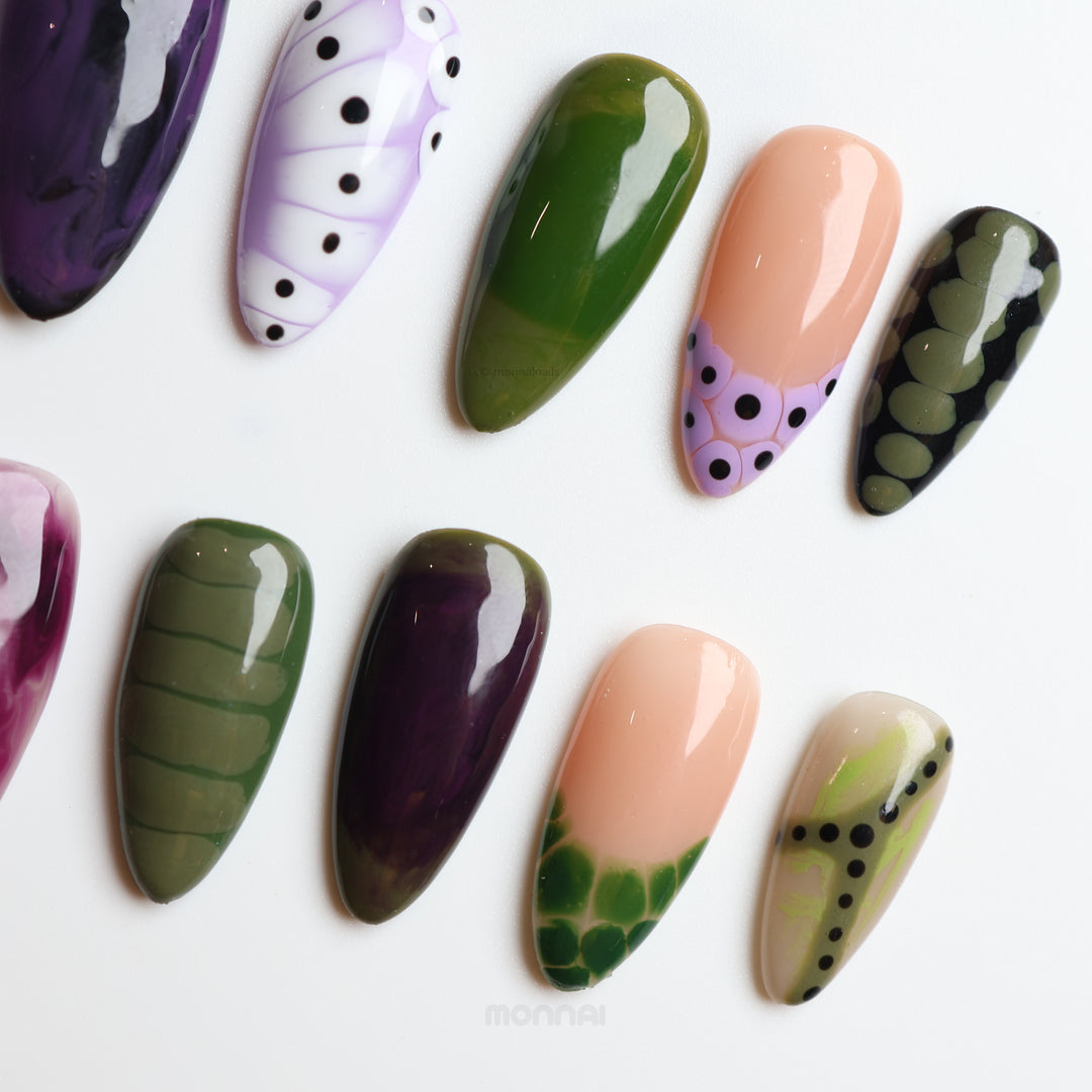 Violet Vines press-on nails with moody purple, olive green and nude glossy marbled, dotted designs shown laid out.